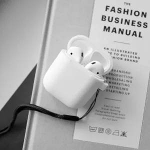 KeyBudz PodSkinz nyckelringsserie AirPods-fodral i vitt med fastsatt handledsrem, visas öppet med hörlurar inuti