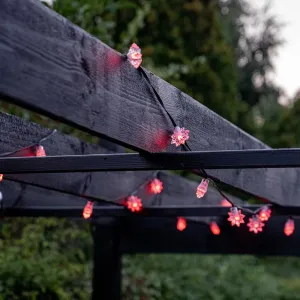 Lite Bulb Moments smarta ljusslinga med stjärnformade rödrosa LED-lampor draperad över en pergola i trä utomhus.