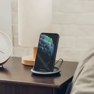 Moshi Lounge Q trådlös laddare som håller en smartphone upprätt på ett sängbord, med laddningsindikator.