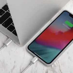 Moshi Integra USB-C till Lightning-kabel ansluten till en bärbar dator och en smartphone som laddas på en ljus marmoryta
