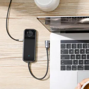 Baseus 6-i-1 USB-C-hubb ansluten till en bärbar dator på ett skrivbord i trä, med kompakt svart rektangulär design