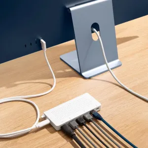 Twelve South StayGo USB-C šakotuvas baltos spalvos su prijungtais laidais ant stalo šalia monitoriaus stovo.