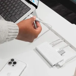 Twelve South StayGo USB-C Hub ant balto stalo, prijungtas prie nešiojamojo kompiuterio, su keliais prijungtais baltais kabeliais.