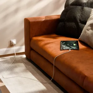 Twelve South USB-C-laddare med integrerad EU-kontakt som laddar en surfplatta bredvid en brun lädersoffa.