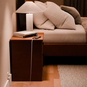 Twelve South PowerCord laddar en smartphone bredvid en säng, med vit kabel och EU-kontakt.