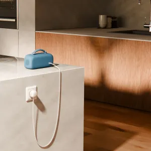 Blå portabel högtalare som drivs via en vit USB-C-kabel i ett modernt kök