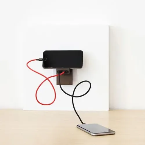 Usbepower Rock Dual USB-A-laddare monterad på väggen med anslutna kablar som laddar en smartphone
