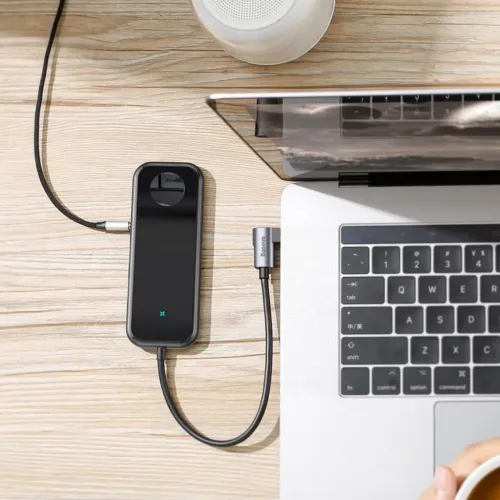 Baseus 6-i-1 USB-C-hubb ansluten till en bärbar dator på ett skrivbord i trä, med kompakt svart rektangulär design