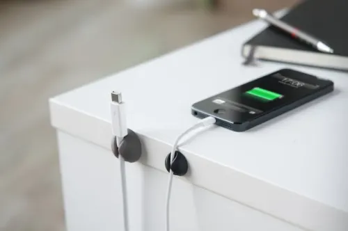 Bluelounge Cable Drop Mini kabelhållare på kanten av ett vitt skrivbord, som håller laddkablarna prydligt på plats.