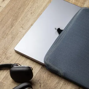 Housse pour ordinateur portable Moshi Pluma 14 pouces gris à chevrons à côté d’un MacBook Pro, avec bordure de fermeture éclair texturée