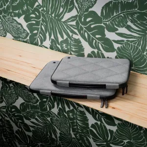 Funda rígida acolchada gris para MacBook Twelve South SuitCase con cremallera, apilada sobre una estantería de madera.