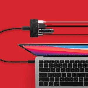 Concentrador USB-C StayGo mini de Twelve South conectado a un portátil con varios cables sobre un fondo rojo.