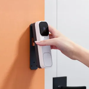Videoportero inteligente Woox en blanco con lente de cámara y botón, montado en una pared y tocado con la mano
