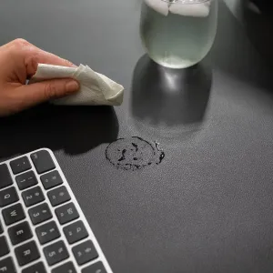 Twelve South DeskPad skrivbordsmatta i svart veganskt läder som torkas ren bredvid ett tangentbord och ett glas vatten
