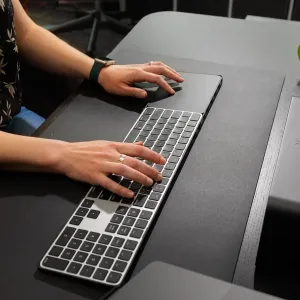 Twelve South DeskPad svart skrivbordsmatta i veganskt läder med tangentbord och händer på en arbetsyta.