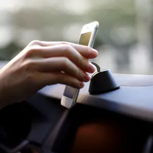 Soporte para teléfono iRing Dock en el salpicadero de un coche, junto a un smartphone, en una configuración de navegación manos libres
