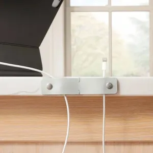 Twelve South CableSnap Stay kabelhanteringsklämma i grått läder som håller en vit laddningskabel på en skrivbordskant