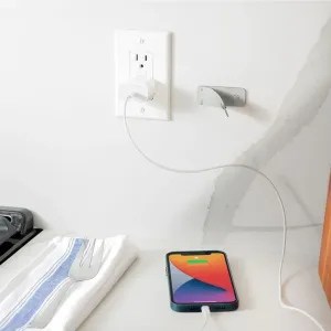 Twelve South CableSnap Stay-kabelhållare monterad bredvid ett vägguttag, där den leder en laddningskabel till en telefon.