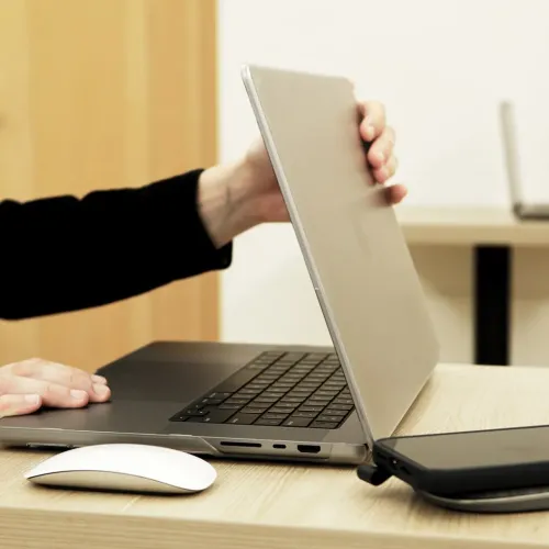 MacBook Pro 16 pouces argent ouvert sur un bureau dans un espace de travail, vu de côté avec une souris à proximité.