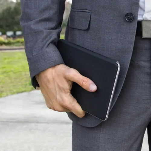 Twelve South SurfacePad-tabletcover i et slankt, sort omslagsdesign, holdt ved en persons side udendørs.