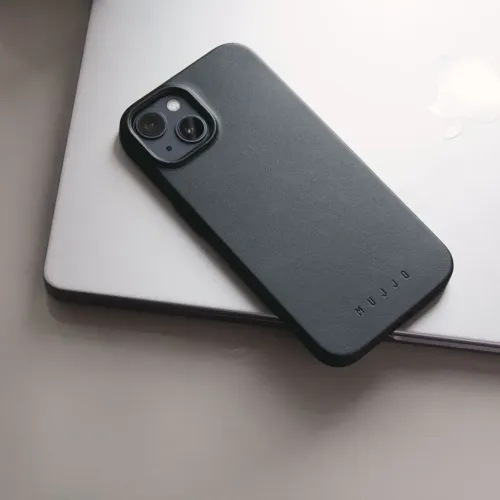 Mujjo black leather iPhone case with raised camera cutout, shown resting on a silver laptop