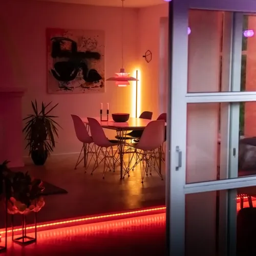 Lite Bulb Moments RGB-LED-nauhavalaistus korotetun lattian reunan alla ruokailuhuoneessa, lämpimässä vaaleanpunais-punaisessa tunnelmavalon hehkussa.