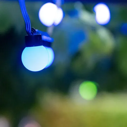 Lite Bulb Moments globelyskæde, der lyser blå-hvidt på et sort kabel, med slørede lys i baggrunden