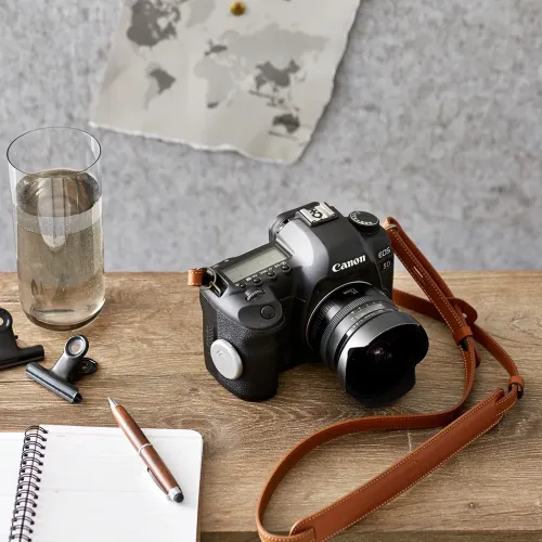 Cámara DSLR Canon EOS 5D con objetivo acoplado y correa marrón sobre una mesa de madera