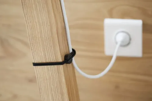 La bande élastique Bluelounge Pixi avec verrou fixe un câble blanc à un poteau en bois pour la gestion des câbles.