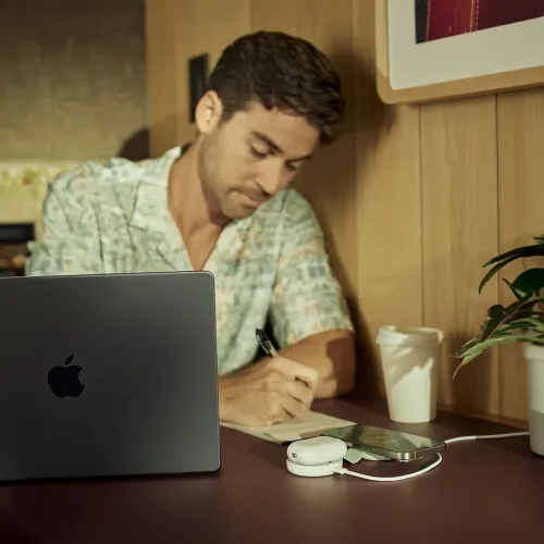 Twelve South ButterFly SE 2-in-1-Qi2-Ladegerät auf einem Schreibtisch, das ein iPhone und AirPods neben einem Notizbuch lädt.